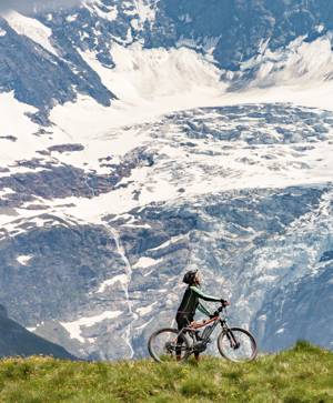 A person riding a bike in the forest with a snow-covered mountain in the back 