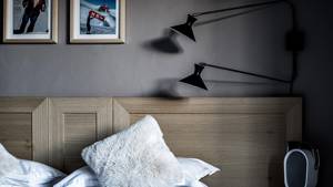 Une photo prise montre une lampe frontale murale et deux portraits au-dessus du lit.