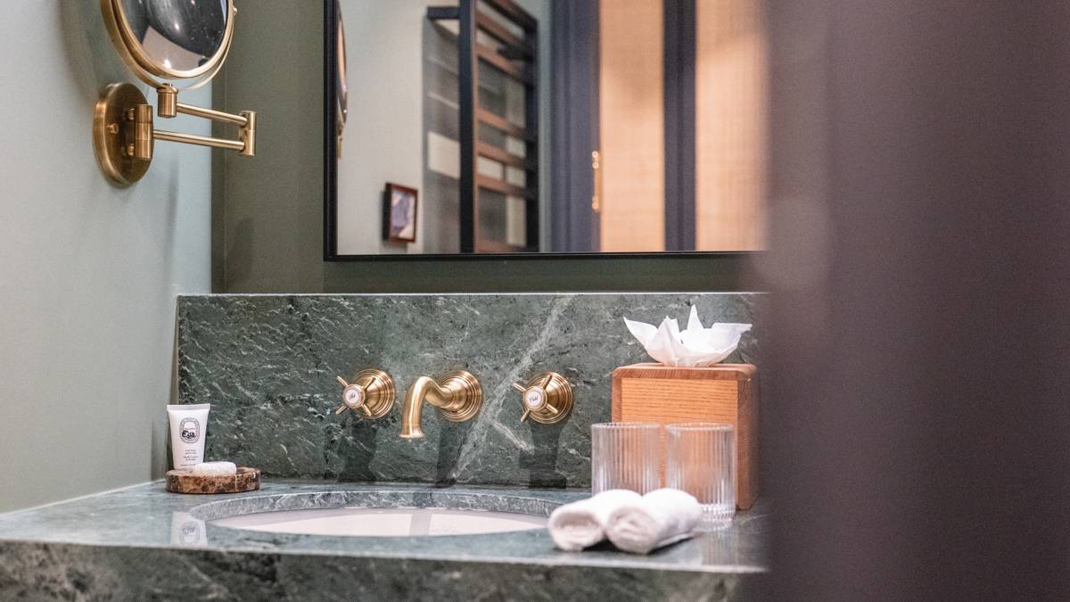 Badezimmer im Le Fitz Roy Val Thorens mit Waschtisch aus grünem Marmor, Messingarmaturen und beleuchtetem Spiegel