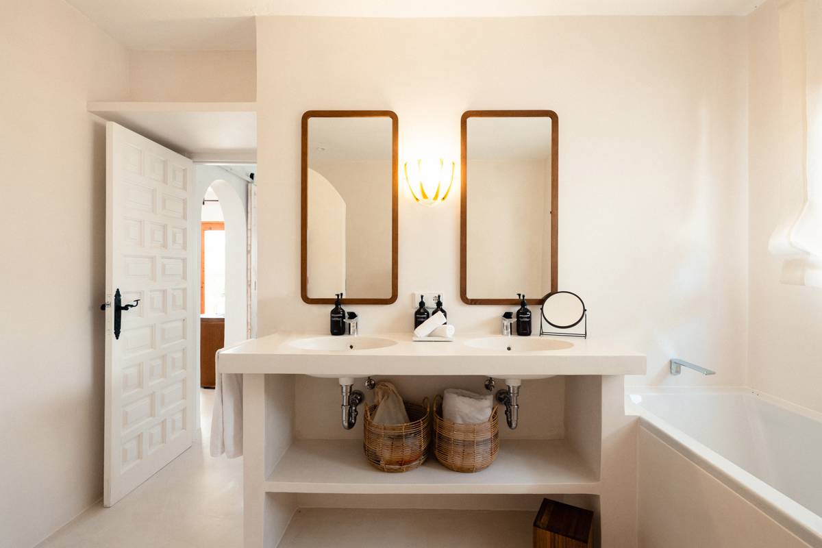 Bright bathroom with double sinks, wooden mirrors, wicker baskets, and a white bathtub, minimalist Mediterranean style.