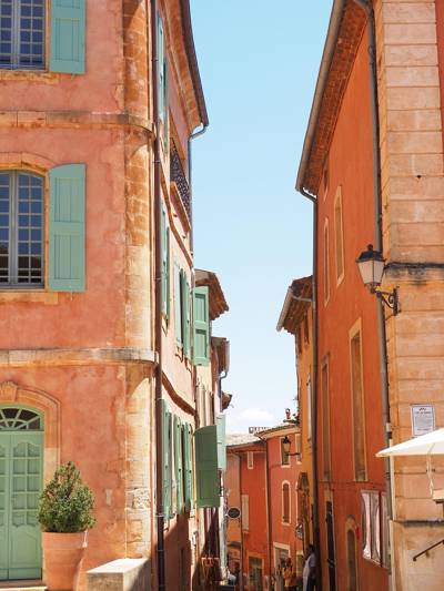 Narrow street in the village of Roussillon, Luberon, lined with ochre and terracotta facades under a bright blue Provençal sky