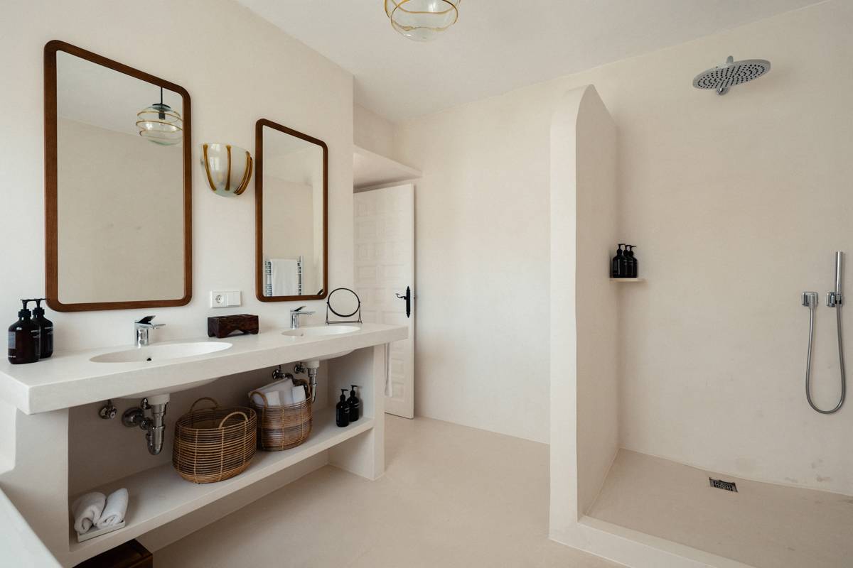 Bathroom with double sinks, large mirrors, open walk-in shower, wicker baskets, and neutral beige tones.