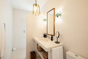 Bright bathroom with a modern sink, wooden mirror, glass pendant light, wicker baskets, and minimal decor in neutral tones.