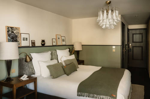 Zimmer im Le Fitz Roy Val Thorens mit salbeigrüner Vertäfelung, weisser Bettwäsche, olivfarbenem Plaid und Murano-Glasleuchter